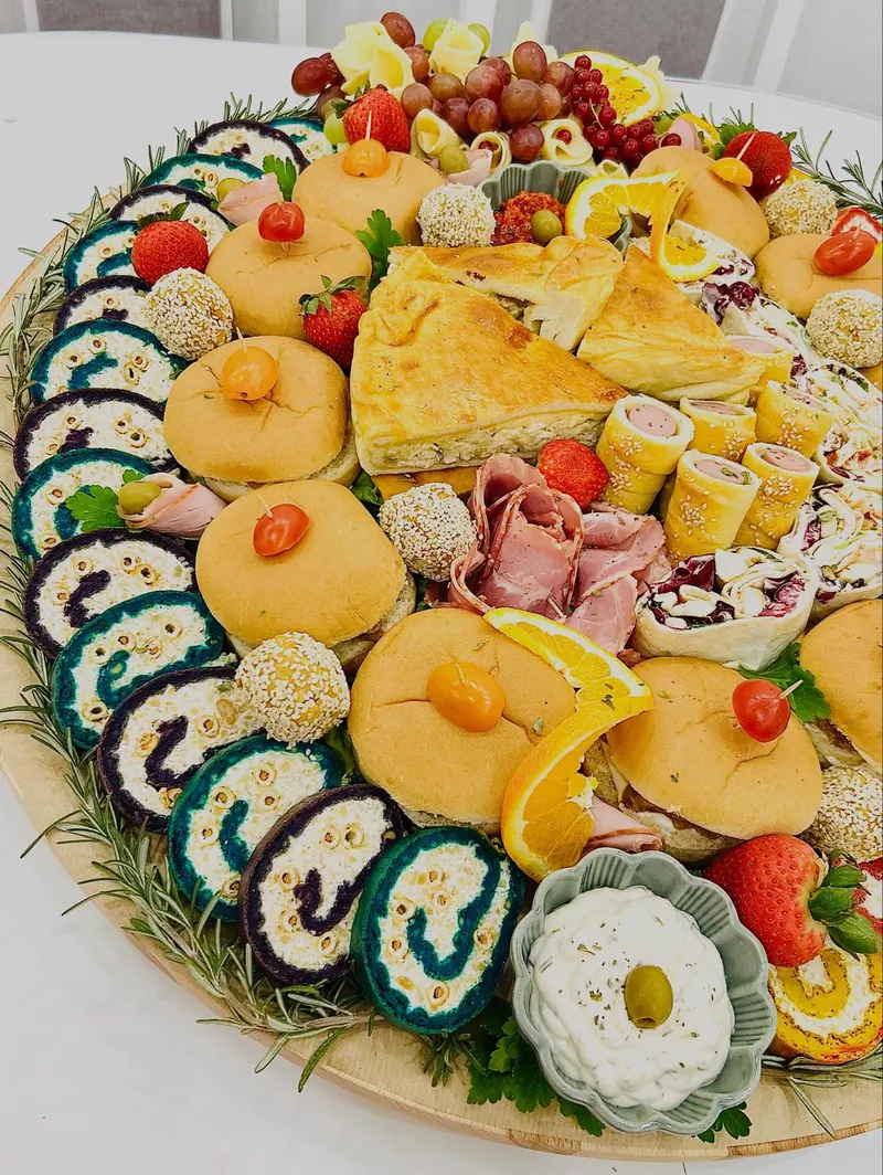 Okrugla slana daska sa šarenim rolatima, pitom, mini burgerima i voćem